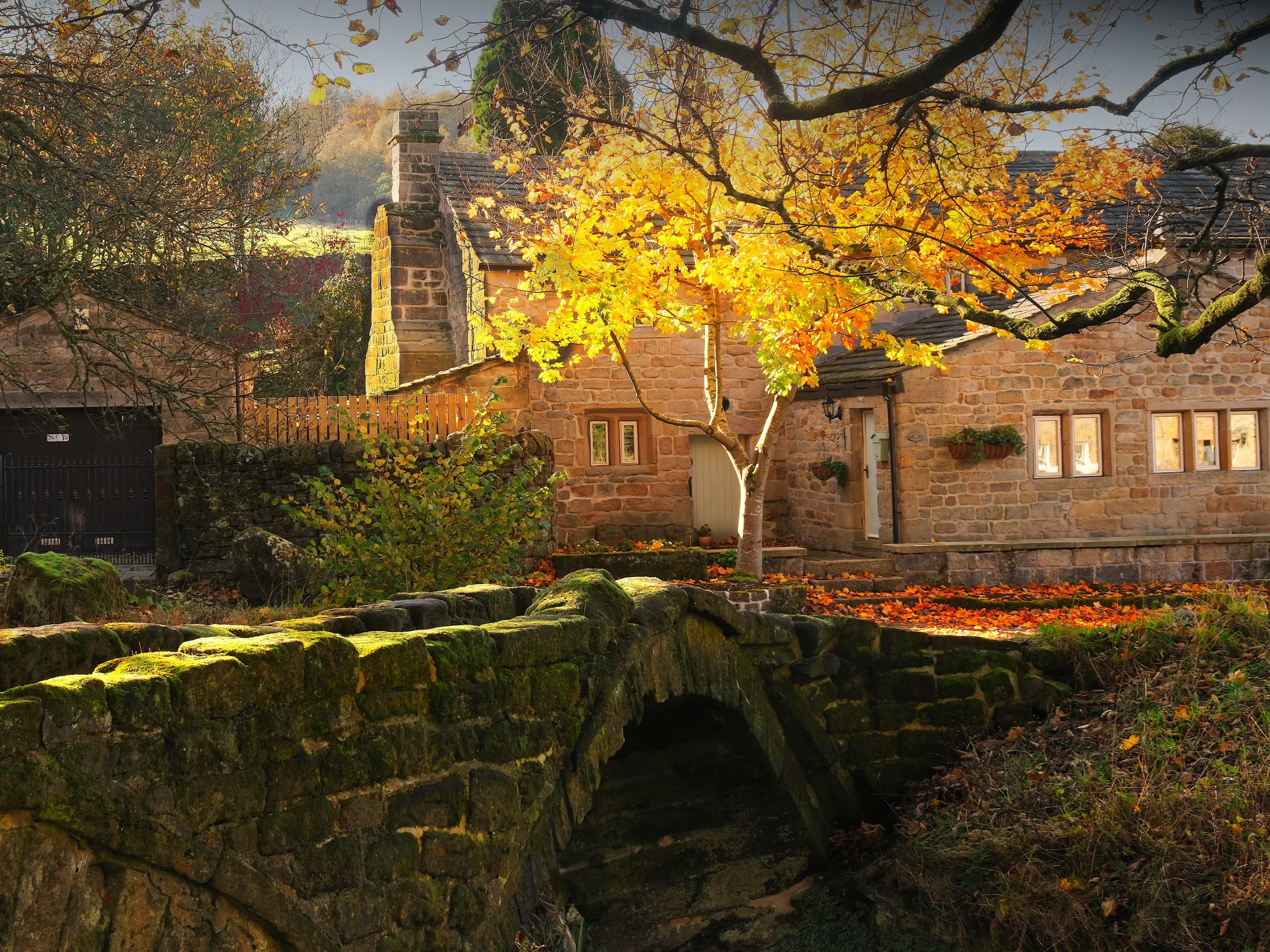 There's a strong chance this image contains the following subjects: tree,  house,  architecture,  landscape,  fall,  lancashire,  bridge,  building. The photographer has provided the following description: Wycoller in a stunning little village near Colne in Lancashire. Right here is the famous Pack Horse Bridge which was used in the film The Railway Children. Jenny Agutter can be seen sitting on the bridge in this iconic film. On the day I took this photo, the sun was extremely bright and overhead, which caused considerable shadows in the image. However, I made the most of it and tried to capture the yellow tree glowing centre of image. I have uploaded another photo of this from a different angle in the snow a few months later. Photographer_name: Chris Michael. Title: Wycoller Pack Horse Bridge. The photographer has provided the following description: Wycoller in a stunning little village near Colne in Lancashire. Right here is the famous Pack Horse Bridge which was used in the film The Railway Children. Jenny Agutter can be seen sitting on the bridge in this iconic film. On the day I took this photo, the sun was extremely bright and overhead, which caused considerable shadows in the image. However, I made the most of it and tried to capture the yellow tree glowing centre of image. I have uploaded another photo of this from a different angle in the snow a few months later. Make: fujifilm. Model: X-T5. Technical: 16-80mm. Published: 2025-09-06 18:35:45