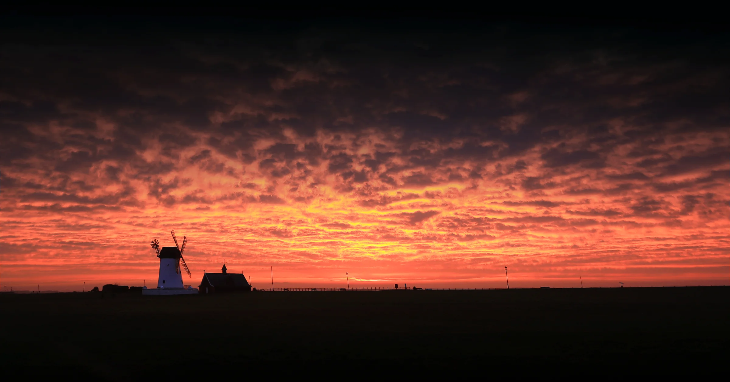 There's a strong chance this image contains the following subjects: sky,  landscape,  sea,  dawn,  lighthouse,  lancashire,  silhouette,  lytham,  windmill,  sunrise. The photographer has provided the following description: 7am and the sky was on fire over Lytham Windmill. Photographer_name: Chris Michael. Title: Sunrise over the Windmill. The photographer has provided the following description: 7am and the sky was on fire over Lytham Windmill. Make: canon. Model: EOS R. Technical: RF16mm wide lens. Published: 2025-09-06 19:10:56