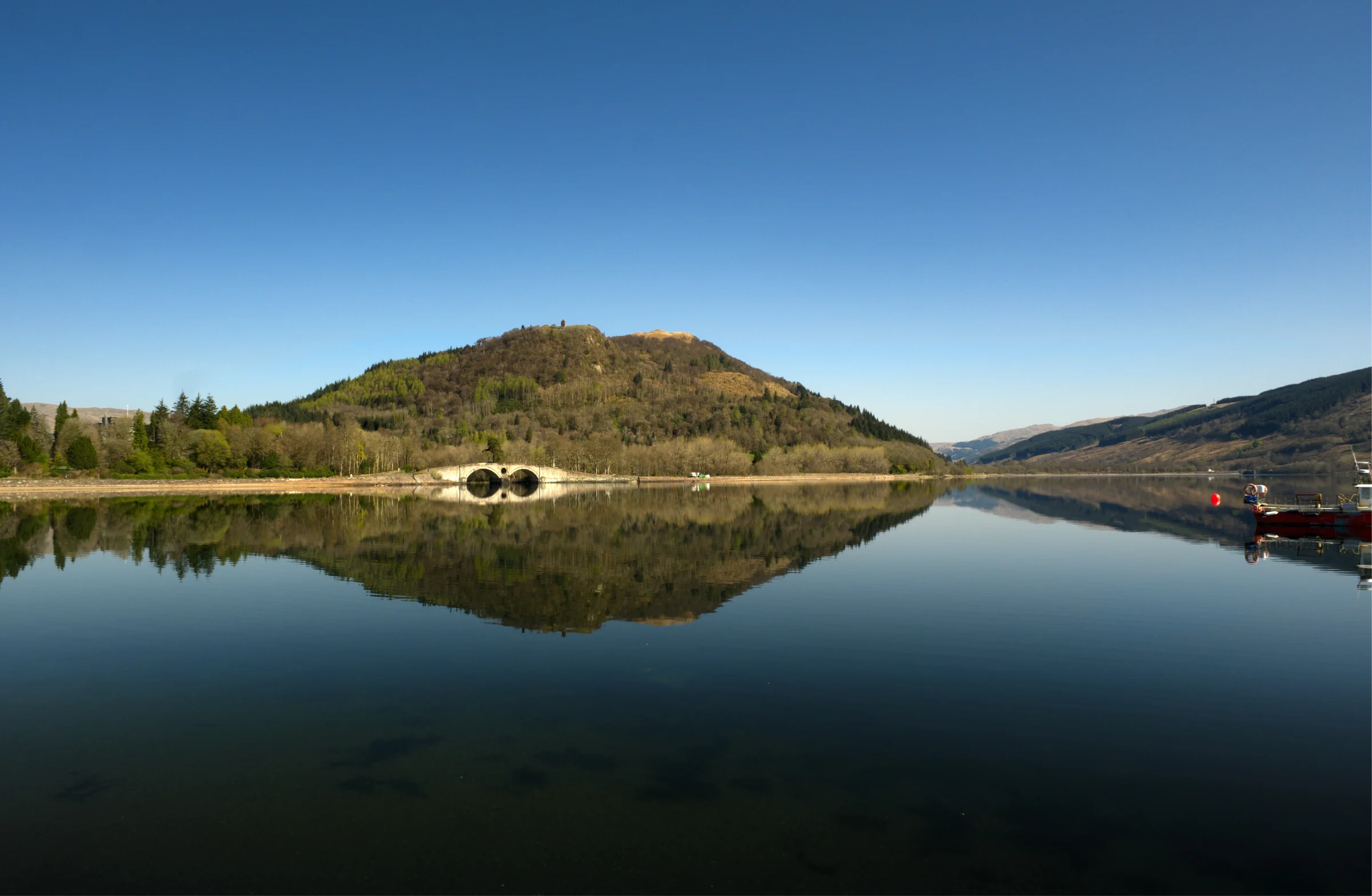 There's a strong chance this image contains the following subjects: sky,  water,  landscape,  lake,  travel,  nature,  reflection,  scotland,  highlands,  scottishhighlands,  inveraray,  reflections. The photographer has provided the following description: This beautiful bridge is seen reflecting in the loch in beautiful Inveraray, Scotland. Photographer_name: Chris Michael. Title: Aray Bridge. The photographer has provided the following description: This beautiful bridge is seen reflecting in the loch in beautiful Inveraray, Scotland. Make: fujifilm. Model: X-T5. Technical: 16-80mm. Published: 2025-09-08 21:50:37
