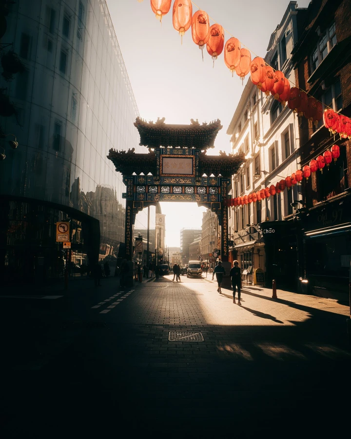 There's a strong chance this image contains the following subjects: architecture,  sky,  street,  city. FOTO has this to say about the photograph: Bathed in warm, rich tones, this stunning sunrise photograph through the ornate gates of London’s Chinatown captures a powerful sense of grandeur and scale. The bustling street beyond hints at vibrant city life awakening, blending tradition and energy in a striking urban moment. Source: https://www.instagram.com/opticalwander/ Photographer_name: Samuel Bassett. Title: 20 Frames of a London Sunrise. FOTO has this to say about the photograph: Bathed in warm, rich tones, this stunning sunrise photograph through the ornate gates of London’s Chinatown captures a powerful sense of grandeur and scale. The bustling street beyond hints at vibrant city life awakening, blending tradition and energy in a striking urban moment. Published: 2025-06-13 15:45:53
