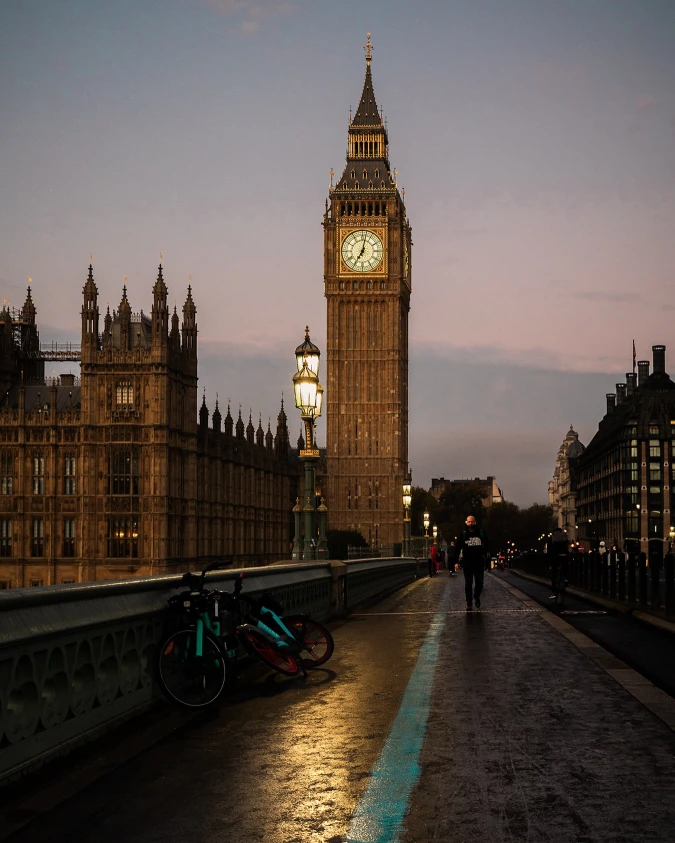 There's a strong chance this image contains the following subjects: architecture,  sky,  street,  light,  city. The photographer has provided the following description: A cinematic evening scene of Big Ben and the Houses of Parliament in London. The wet pavement reflects the glow of streetlights as a jogger moves through the frame. Bicycles rest against the bridge railing, adding to the urban atmosphere. The sky fades into twilight, casting a moody yet golden ambiance over the city. FOTO has this to say about the photograph: Bathed in the rich, golden tones of sunset, this captivating photograph of Big Ben is alive with warmth and wonder. The shimmering reflections on the wet pavement draw the eye forward, inviting you to step into the scene and wander the timeless streets of London. Truly inspiring. Source: https://www.instagram.com/rems.visuals/ Photographer_name: Reumel. The photographer has provided the following description: A cinematic evening scene of Big Ben and the Houses of Parliament in London. The wet pavement reflects the glow of streetlights as a jogger moves through the frame. Bicycles rest against the bridge railing, adding to the urban atmosphere. The sky fades into twilight, casting a moody yet golden ambiance over the city. FOTO has this to say about the photograph: Bathed in the rich, golden tones of sunset, this captivating photograph of Big Ben is alive with warmth and wonder. The shimmering reflections on the wet pavement draw the eye forward, inviting you to step into the scene and wander the timeless streets of London. Truly inspiring. Published: 2025-06-13 16:08:26